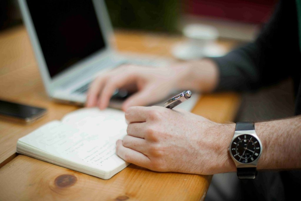 Handwriting notes – Person taking notes beside open laptop.